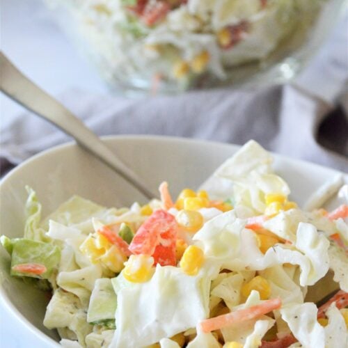 Greek yogurt coleslaw with corn and peppers in a white bowl, with a glass bowl of slaw behind it