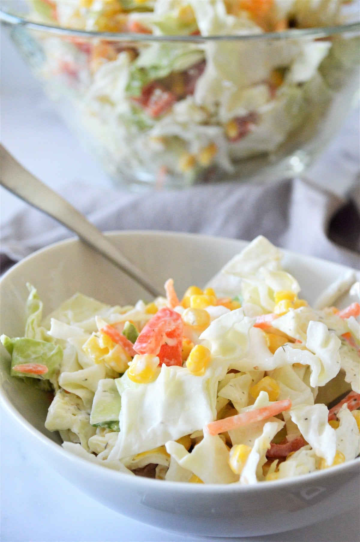 Greek yogurt coleslaw with corn and peppers in a white bowl, with a glass bowl of slaw behind it