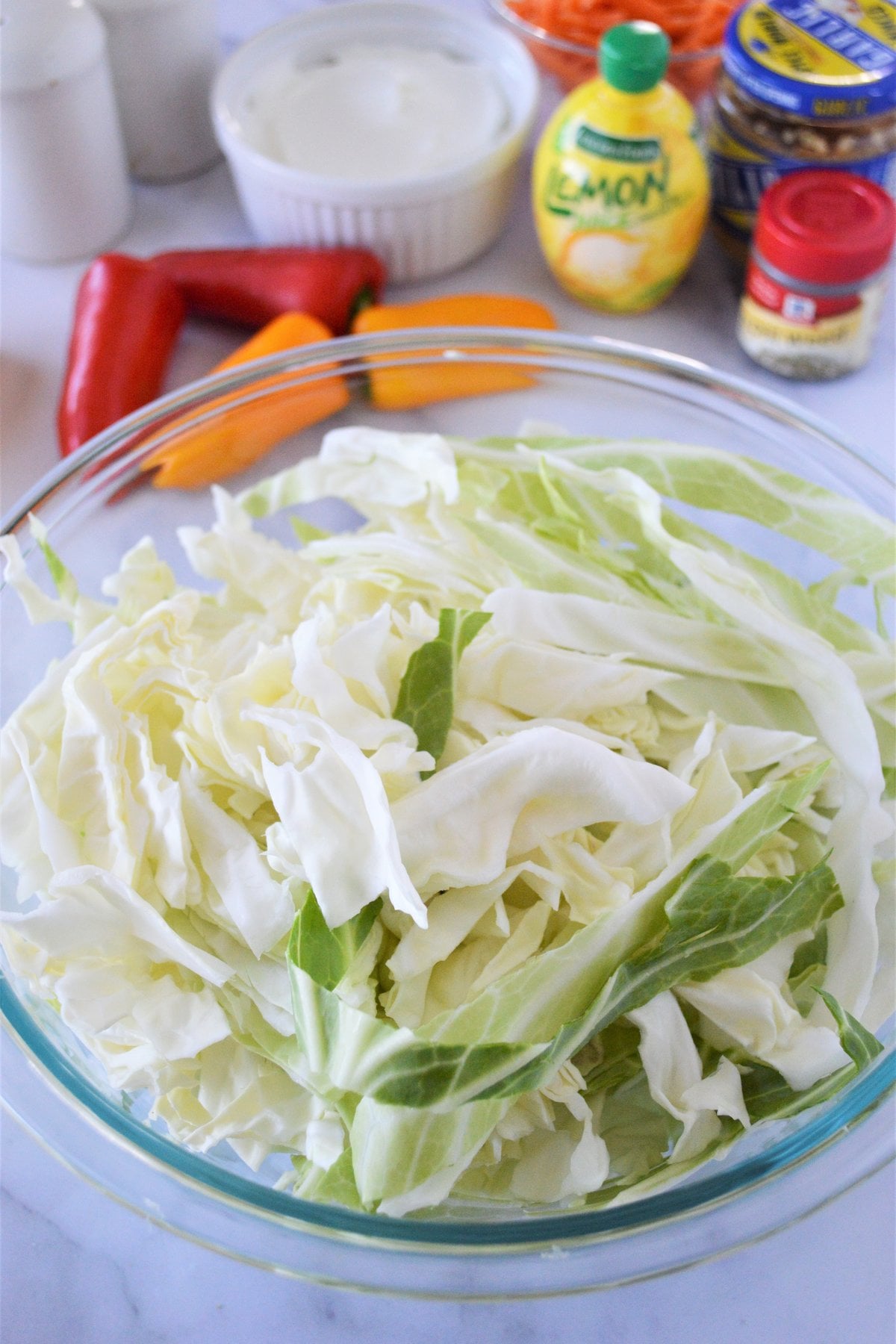 thinly sliced green cabbage in a large glass bowl for healthy coleslaw