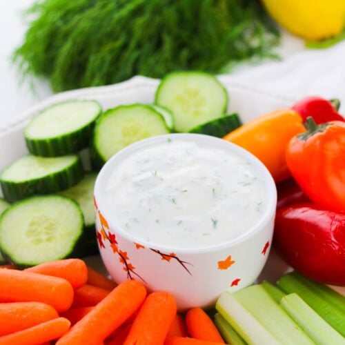 Greek yogurt dill dip in a bowl surrounded by cucumbers, carrots, celery and sweet peppers