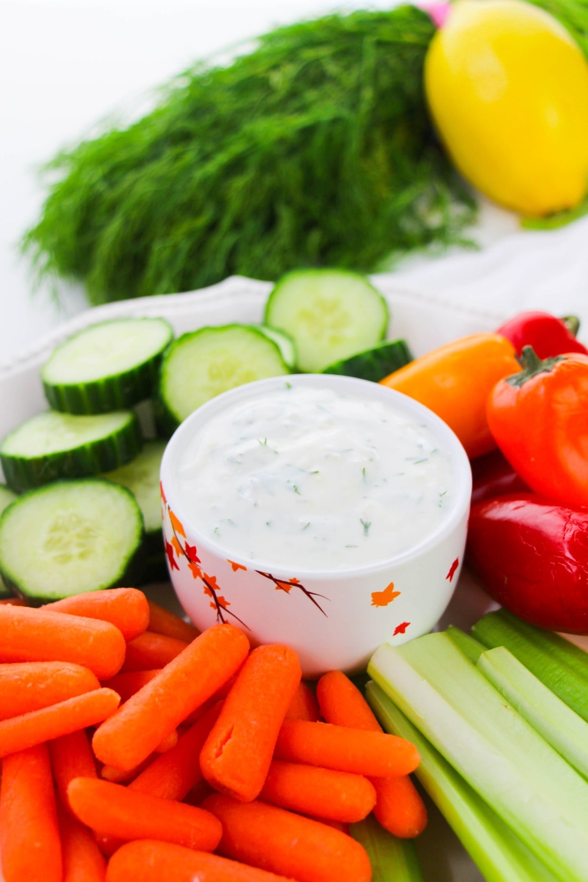 Greek yogurt dill dip in a bowl surrounded by cucumbers, carrots, celery and sweet peppers