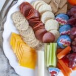 Healthy charcuterie board with grapes, crackers, and light cheeses, viewed from above.