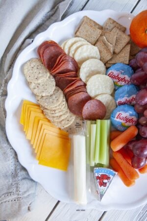 Healthy charcuterie board with grapes, crackers, and light cheeses, viewed from above.