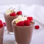 Two chocolate peanut butter cottage cheese pudding cups topped with whipped cream and raspberries.