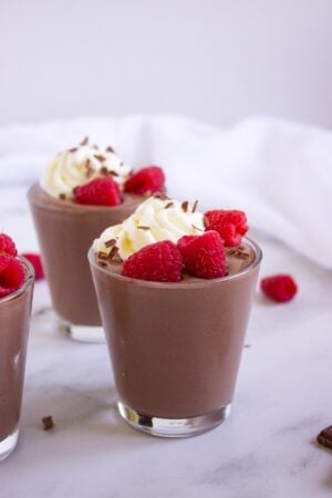 Two chocolate peanut butter cottage cheese pudding cups topped with whipped cream and raspberries.