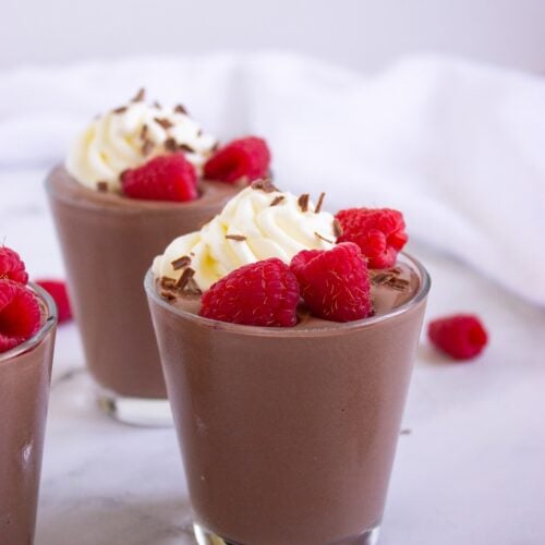 Two chocolate peanut butter cottage cheese pudding cups topped with whipped cream and raspberries.