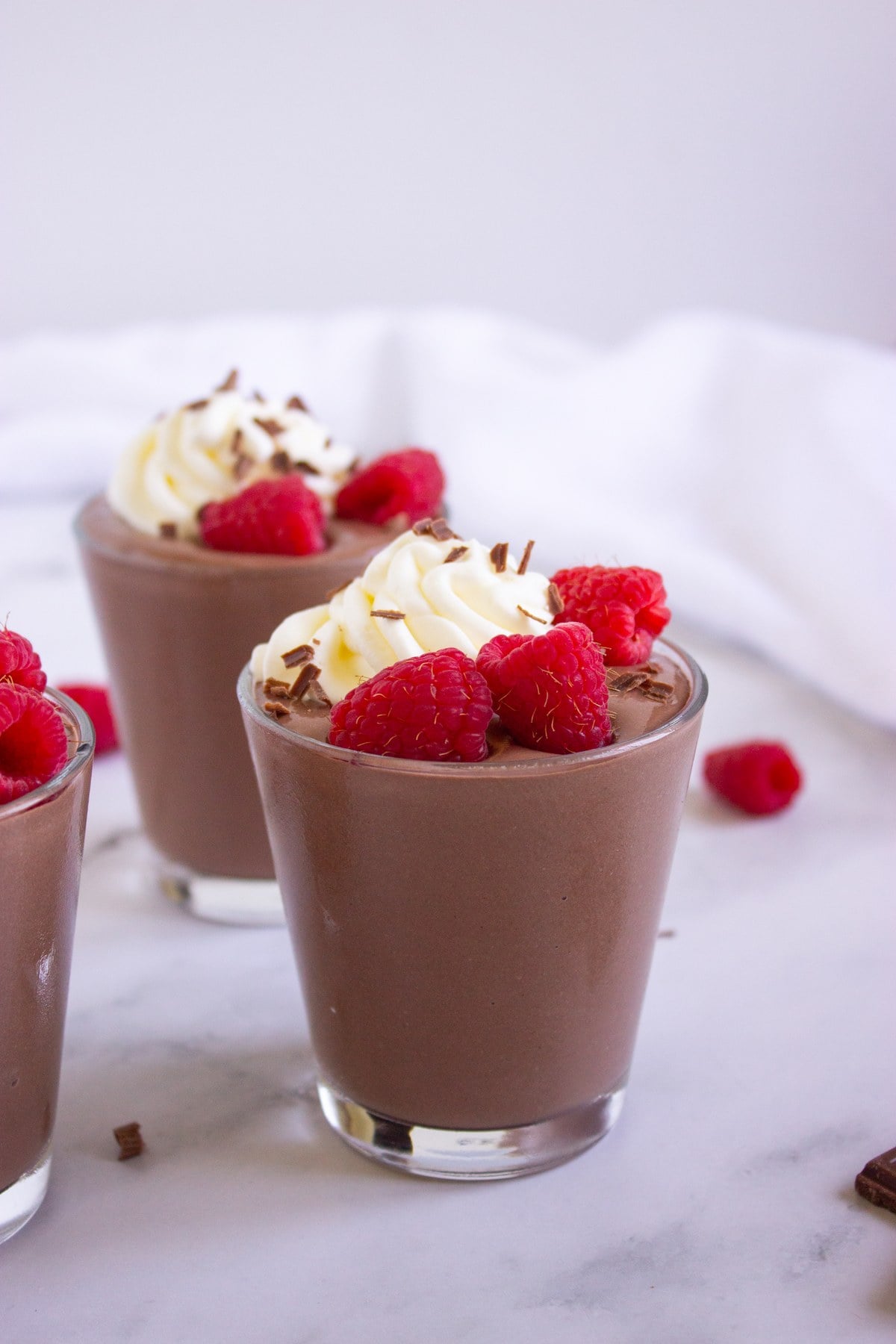 Two chocolate peanut butter cottage cheese pudding cups topped with whipped cream and raspberries.