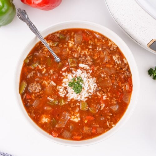 Bowl of crockpot stuffed pepper soup topped with rice and parsley, with the crockpot behind.
