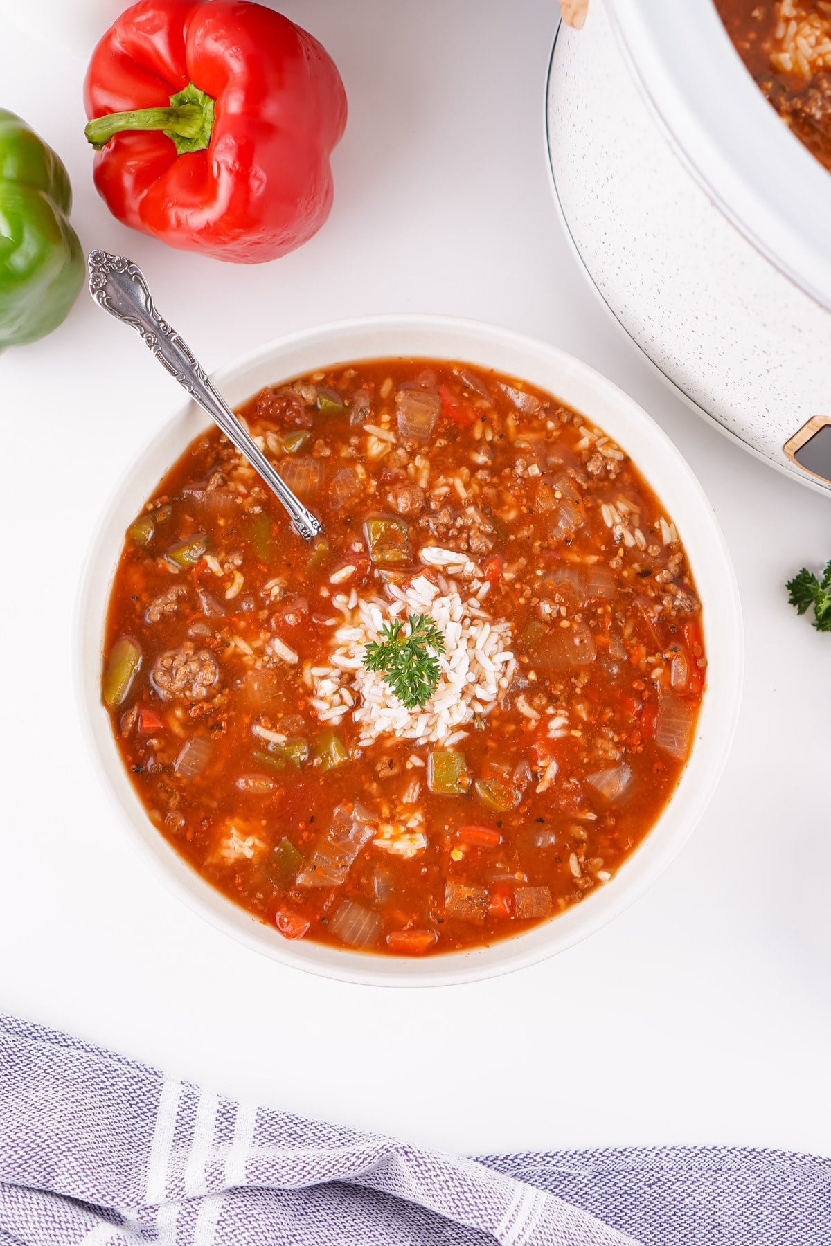 Bowl of crockpot stuffed pepper soup topped with rice and parsley, with the crockpot behind.