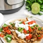 Pork carnitas on a tortilla with toppings, with the Instant Pot behind.