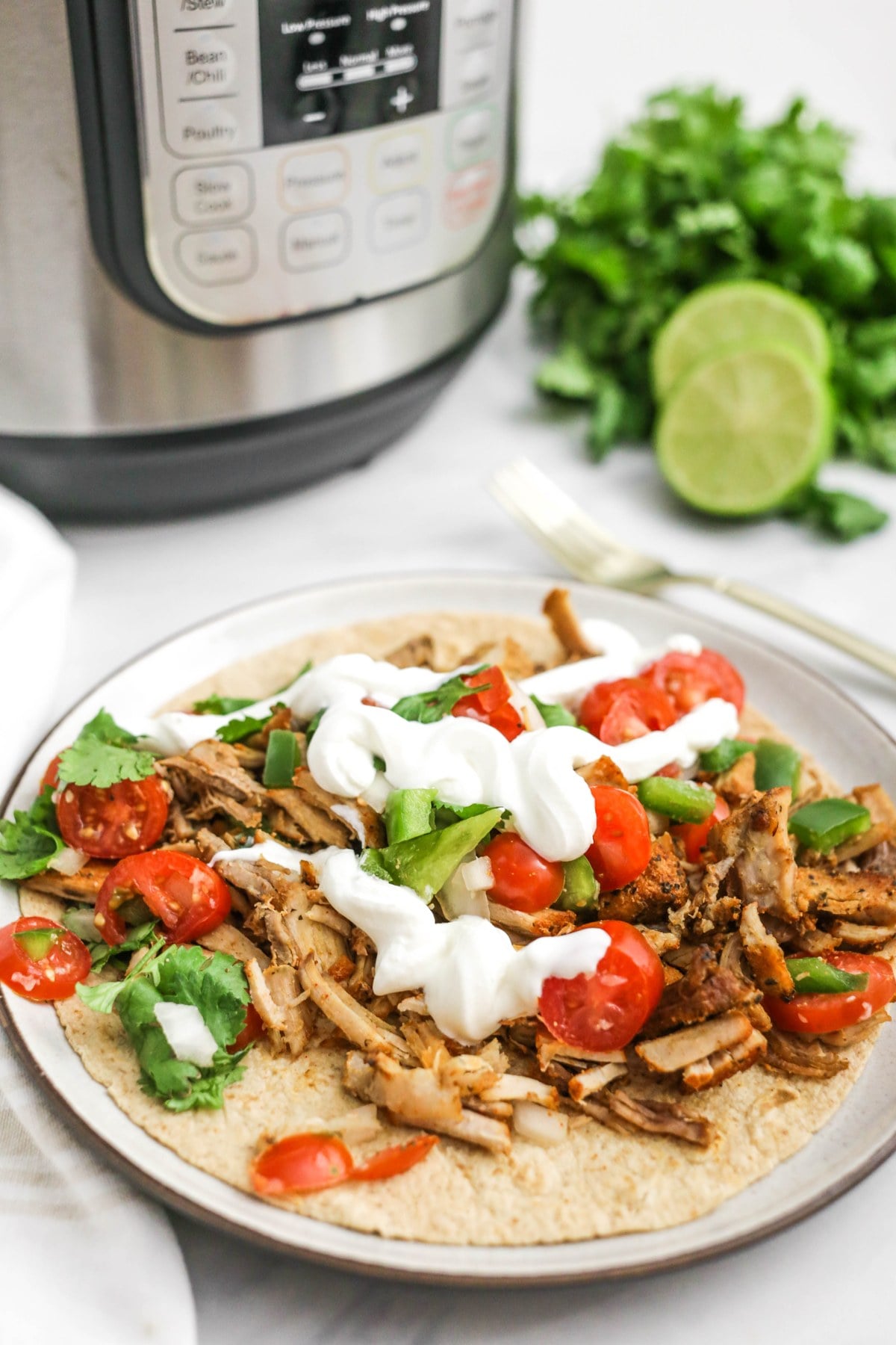 Pork carnitas on a tortilla with toppings, with the Instant Pot behind.