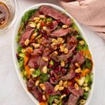 Winter steak salad with Brussels sprouts and pomegranate on an oval platter, viewed from above.