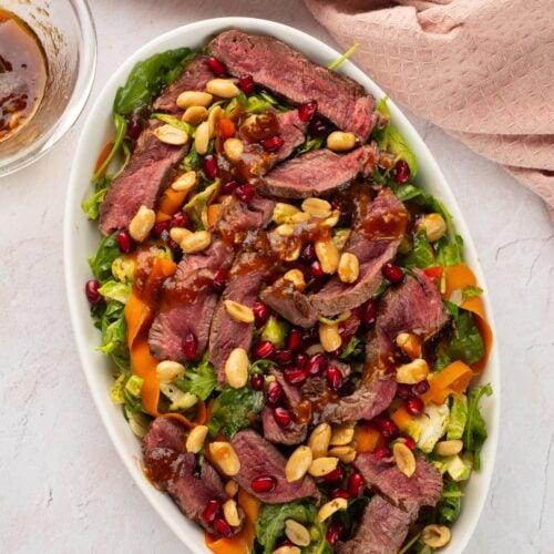 Winter steak salad with Brussels sprouts and pomegranate on an oval platter, viewed from above.