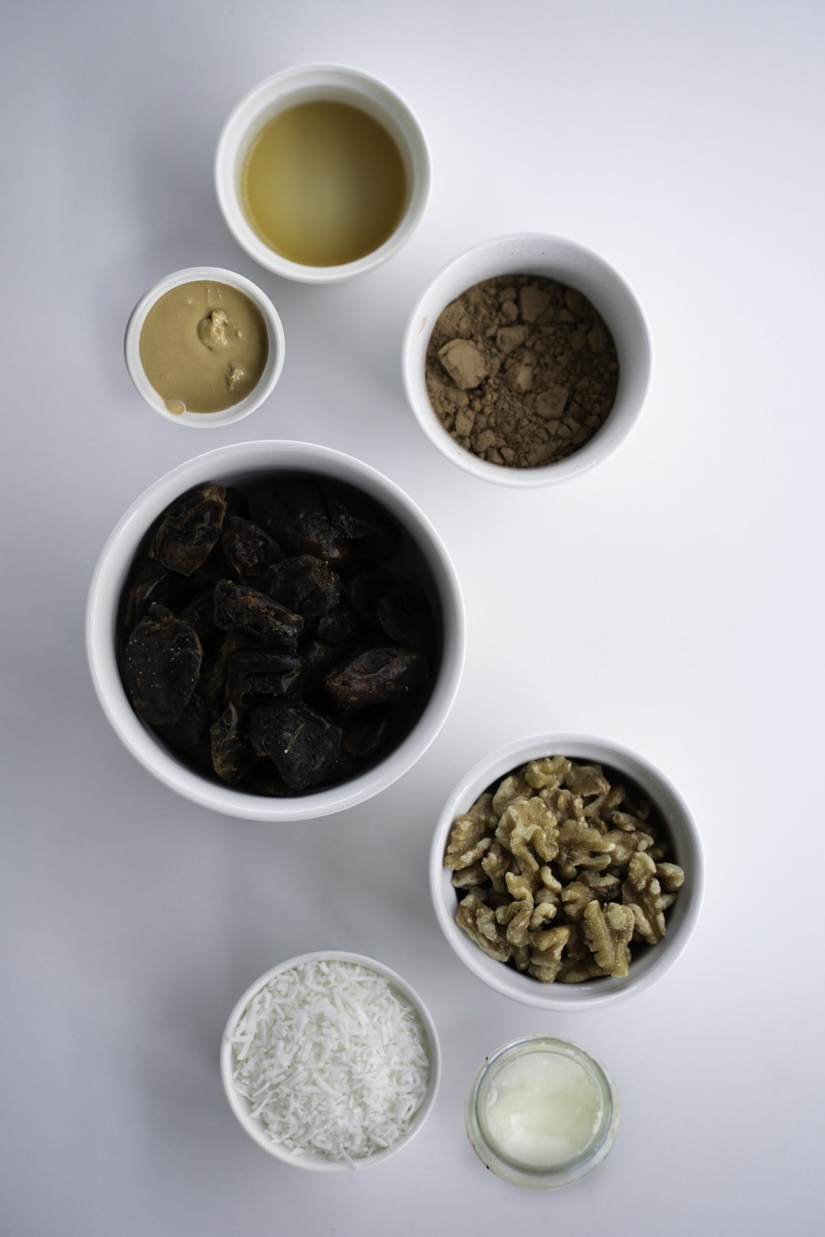 Ingredients in bowls for no-bake date brownies and peanut butter caramel, viewed from above.