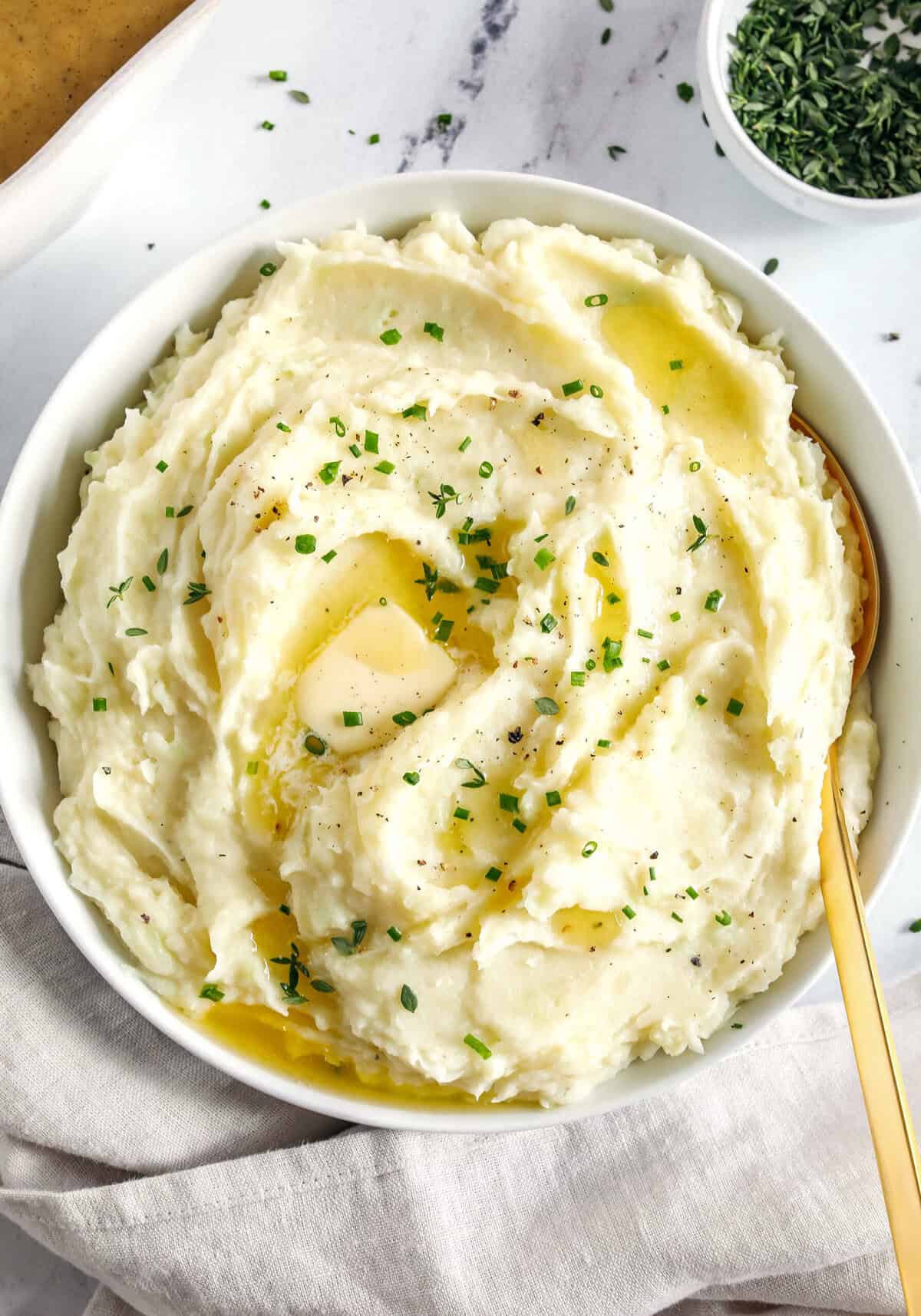 A bowl of mashed potatoes topped with a pat of butter, melted butter, and fresh chives, perfect as an easy Thanksgiving side.