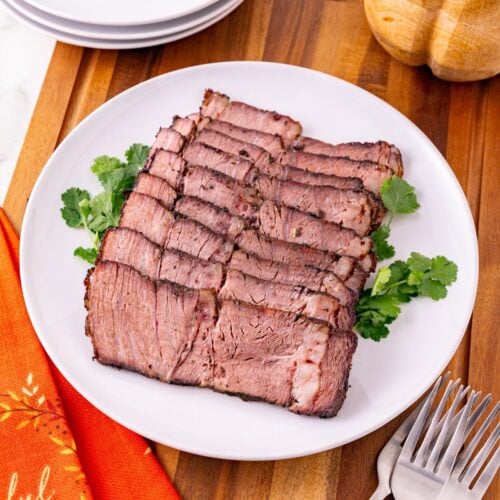 sliced reverse sear chuck roast on a white platter with a fall table setting