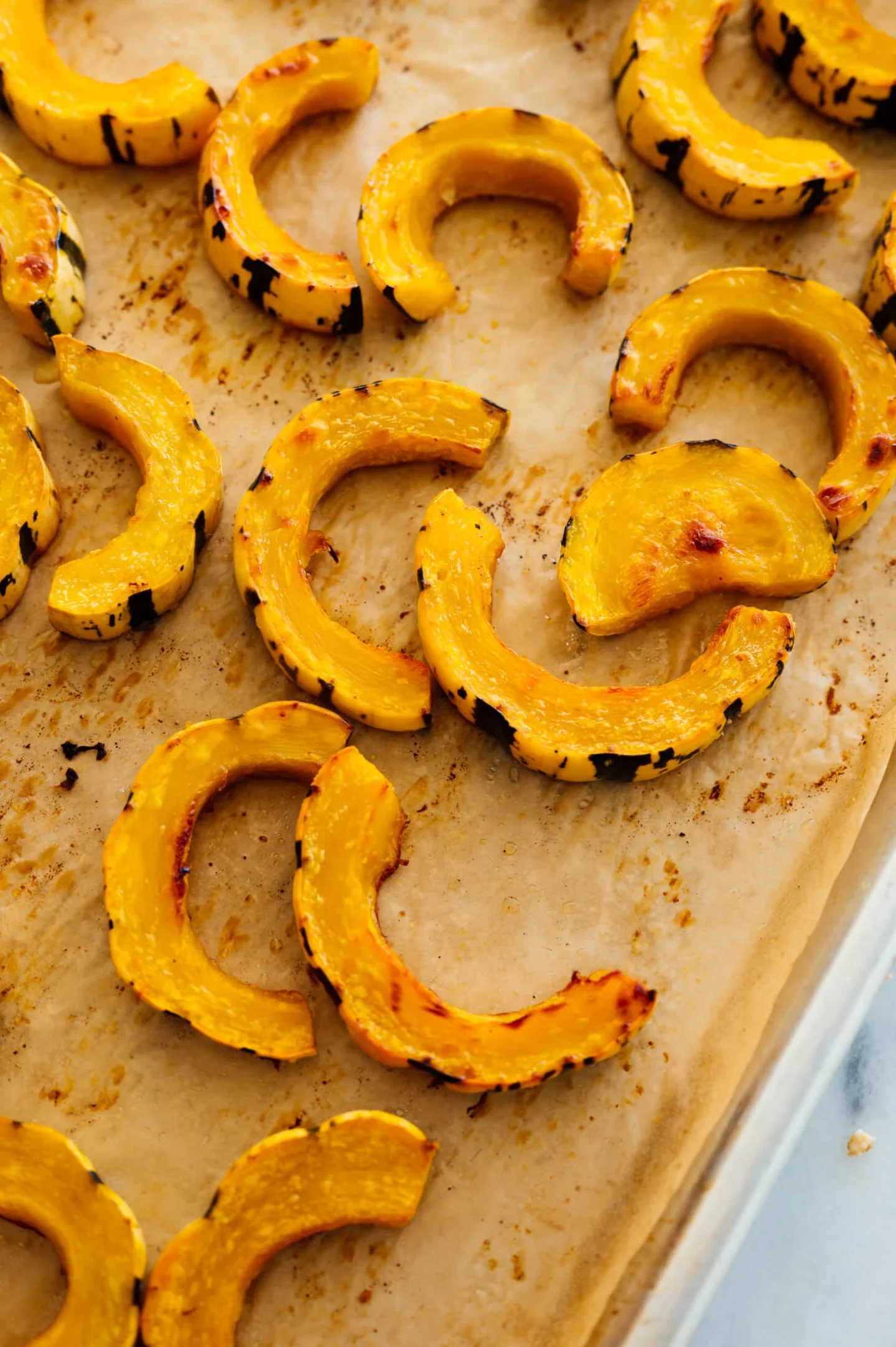 Roasted slices of delicata squash on a parchment-lined baking sheet, perfect as an easy thanksgiving recipe.