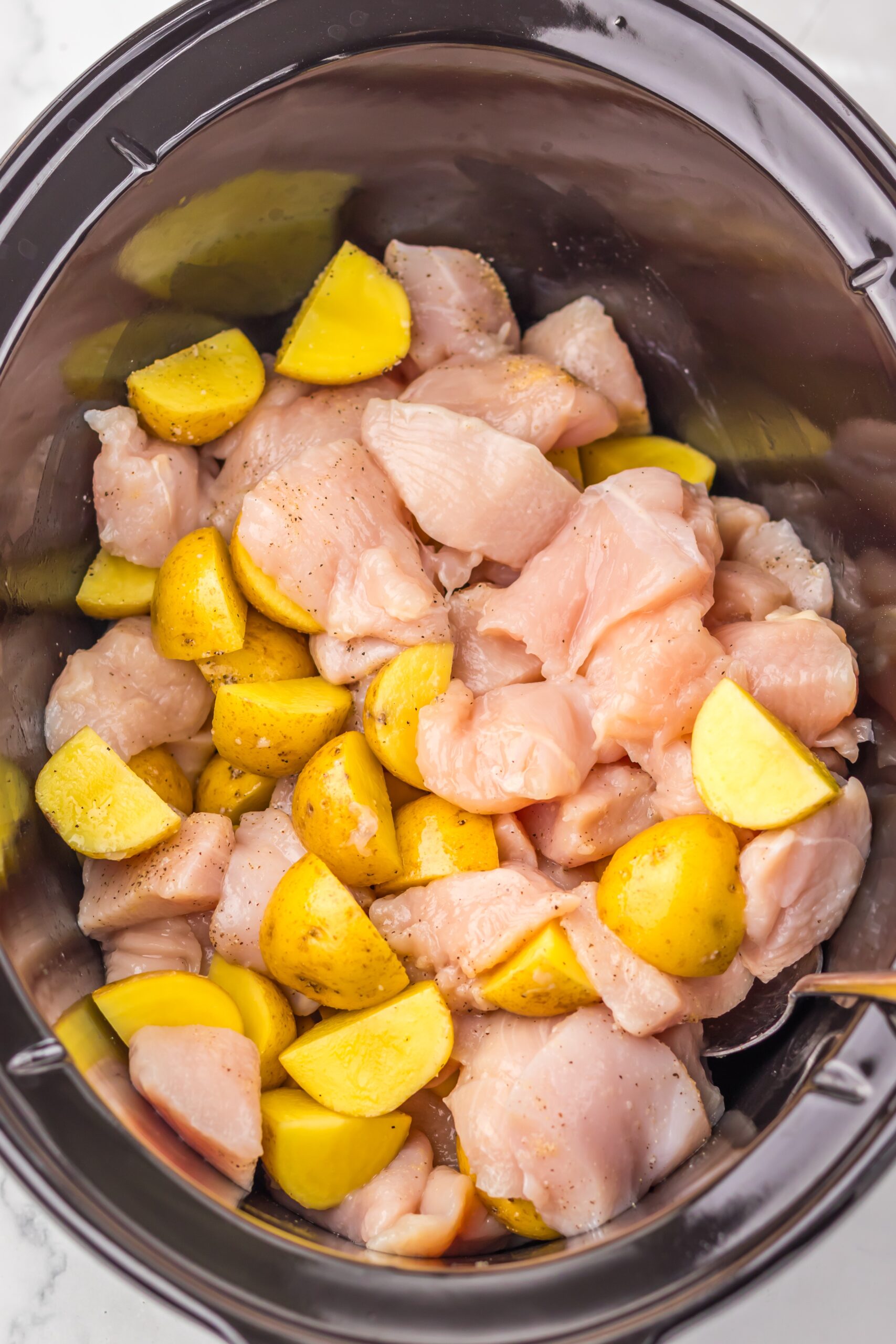 Potatoes and seasoned chicken layered in the slow cooker.
