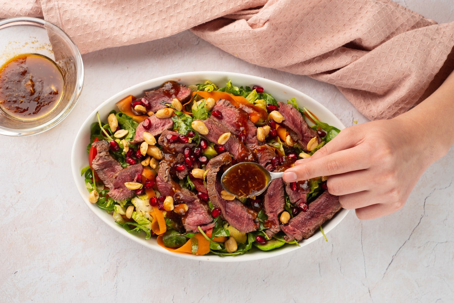 Pomegranate seeds and peanuts topping the salad as dressing is drizzled over it.